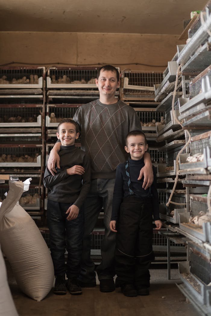 who-we-are Full body of happy father and sons smiling while standing together near cages at poultry farm