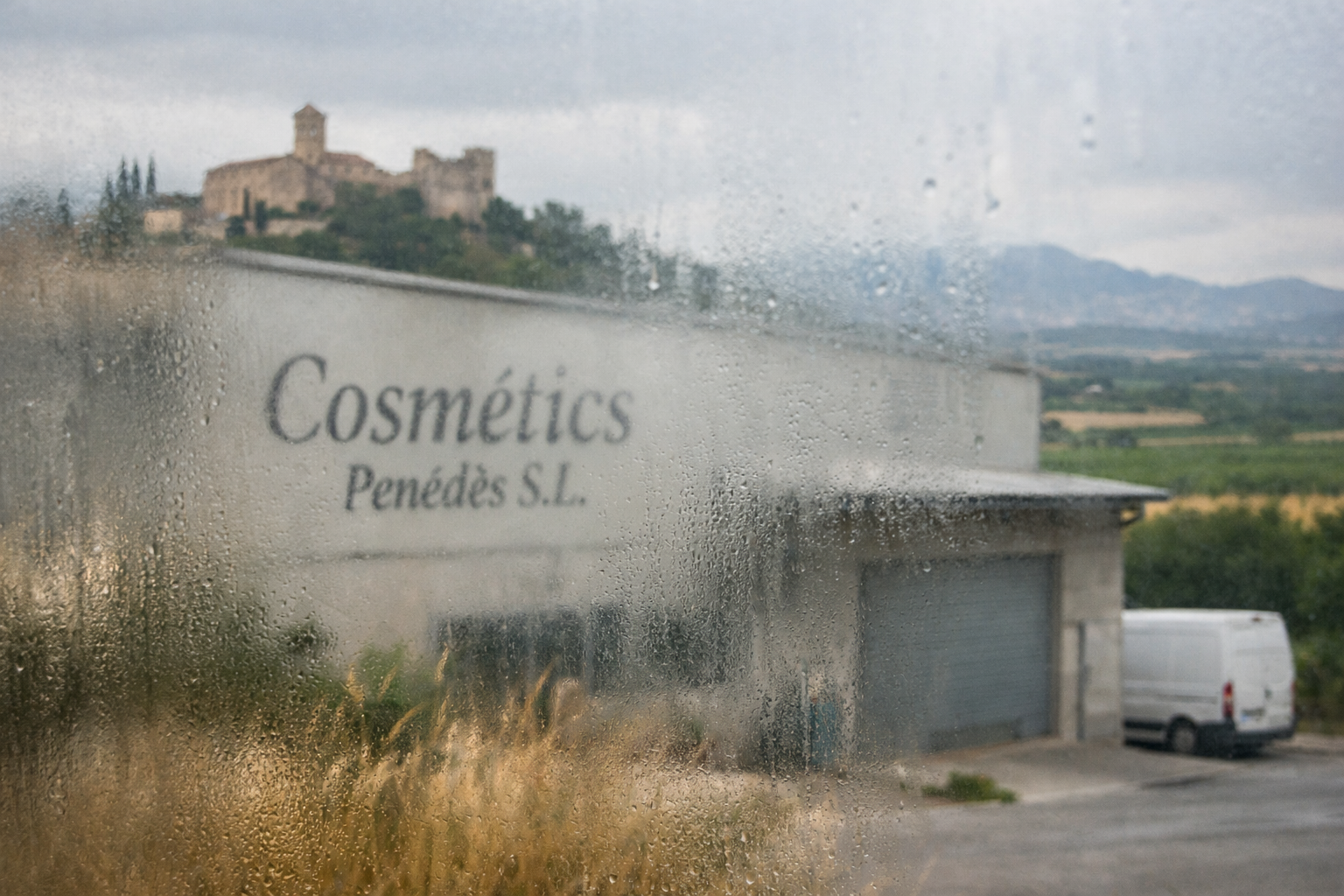 Empresa de cosmética en el Penedès vista a través de un cristal empañado, con el edificio y su entorno rural desenfocados que dificultan su visibilidad- Molt Bé